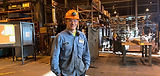 Smiling intern in blues and hard hat inside Scot Forge factory.