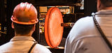 Workers observe a large, hot metal disc in a manufacturing setting, Scot Forge.