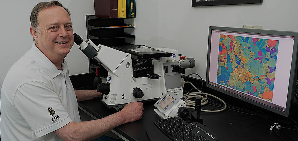 Man smiling near microscope, computer showing colorful scientific data analysis.